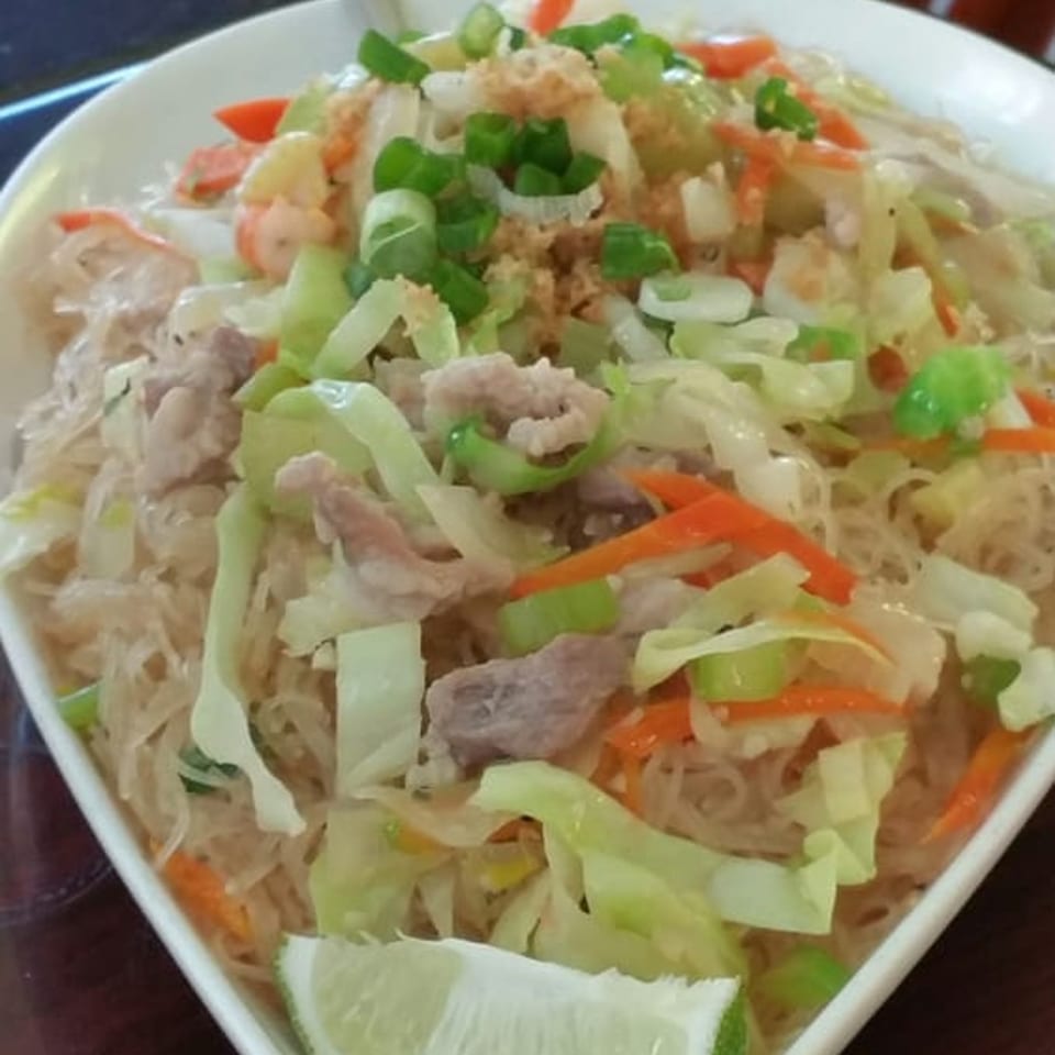 A white bowl of Filipino Pancit Bihon with noodles, pork, shrimp, and vegetables, garnished with lime.