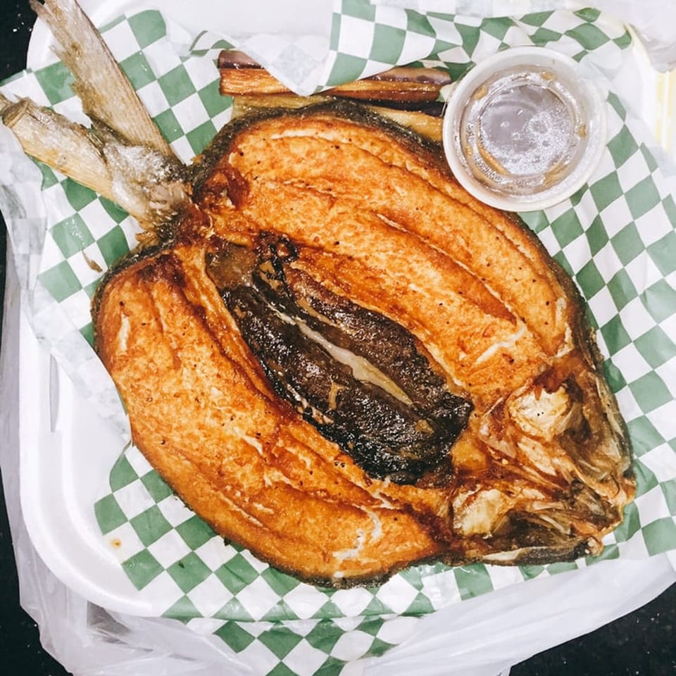 A whole fried milkfish, or Daing na Bangus, on green and white checkered paper with a dipping sauce.