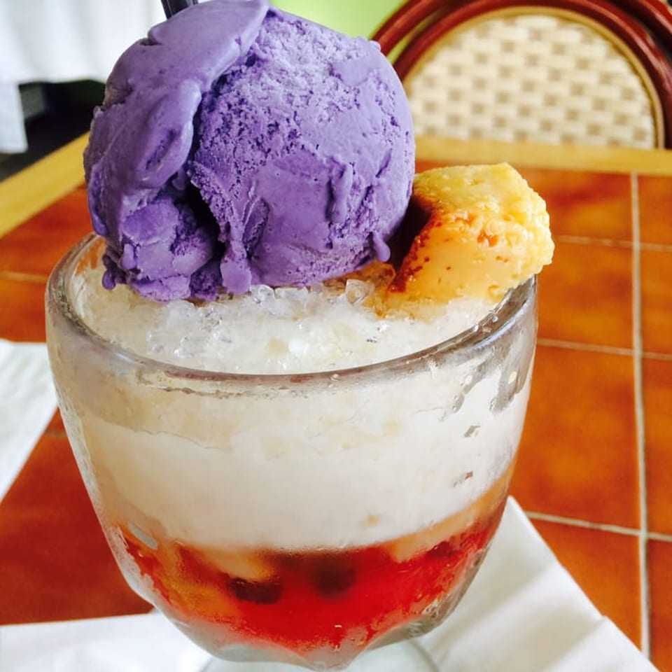 Halo-halo dessert with purple ube ice cream, yellow ice cream, shaved ice, and red syrup.