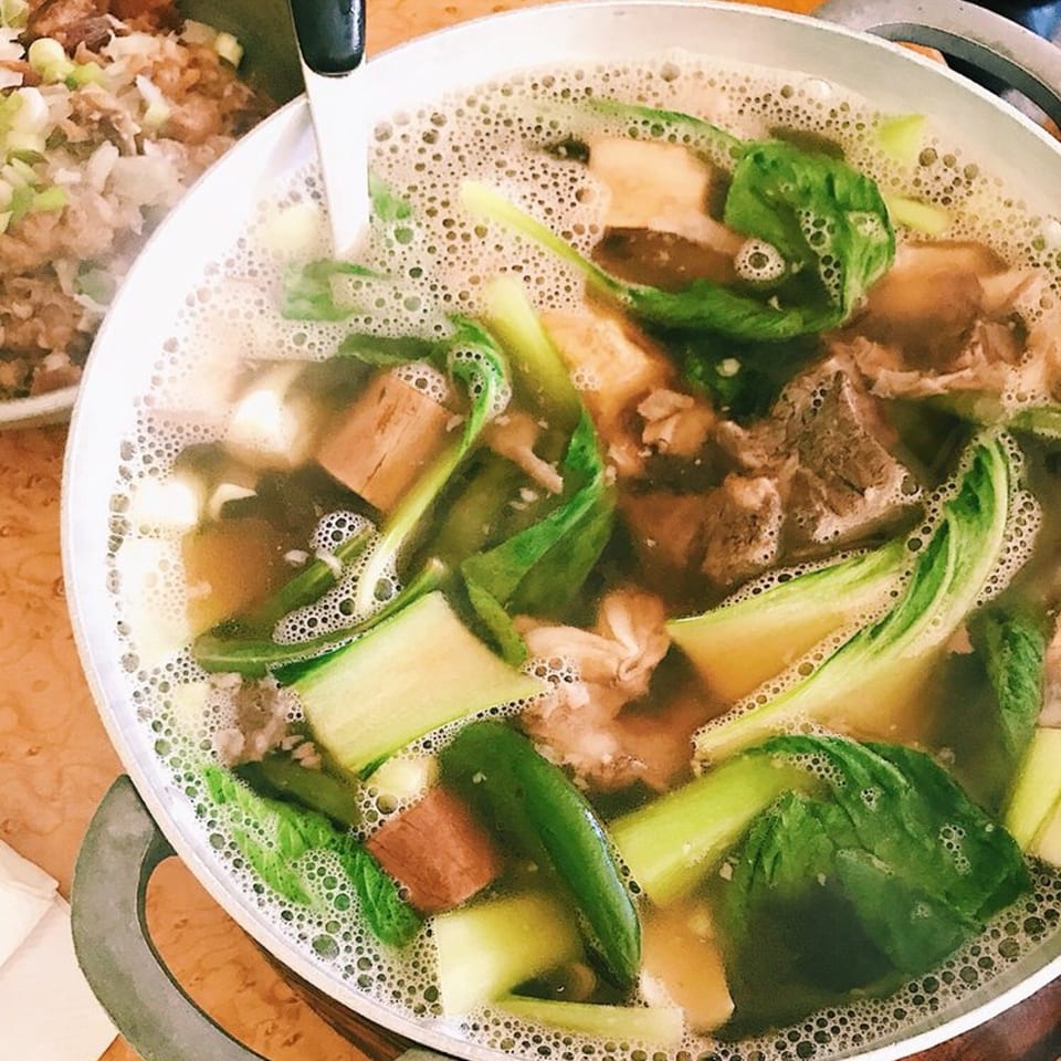 Close-up of a bubbling pot of Filipino Sinigang soup with meat, bok choy, and other vegetables.