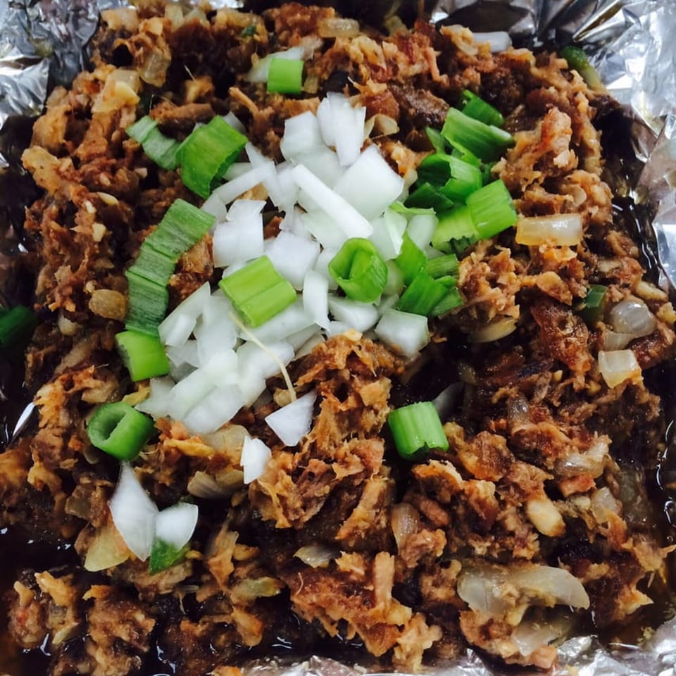Close-up of Tina's Filipino Cuisine sisig, a savory dish topped with chopped white and green onions.